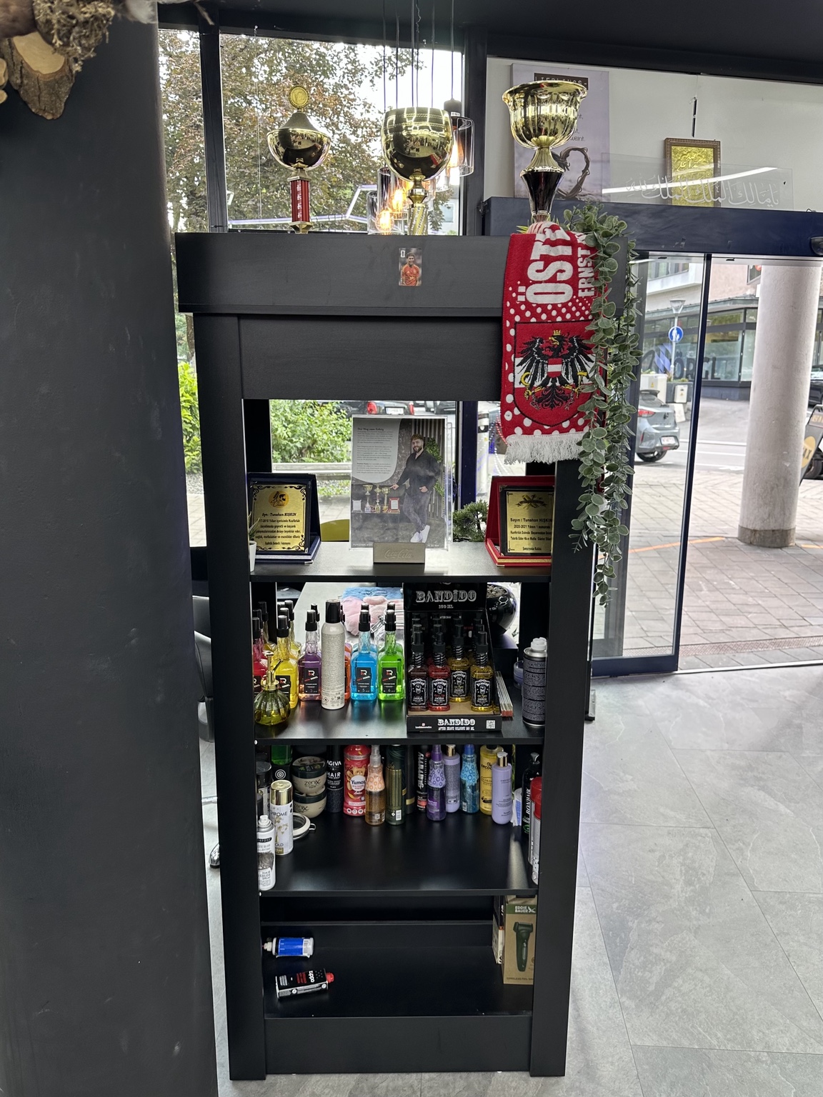 Schwarzes Produktregal mit Pflegeprodukten und goldenen Pokalen