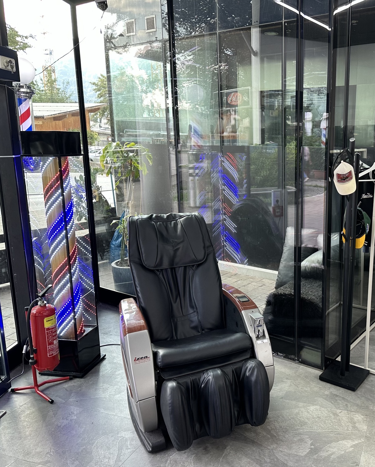 Massagesessel neben beleuchteter Barber-Pole an der Glasfront